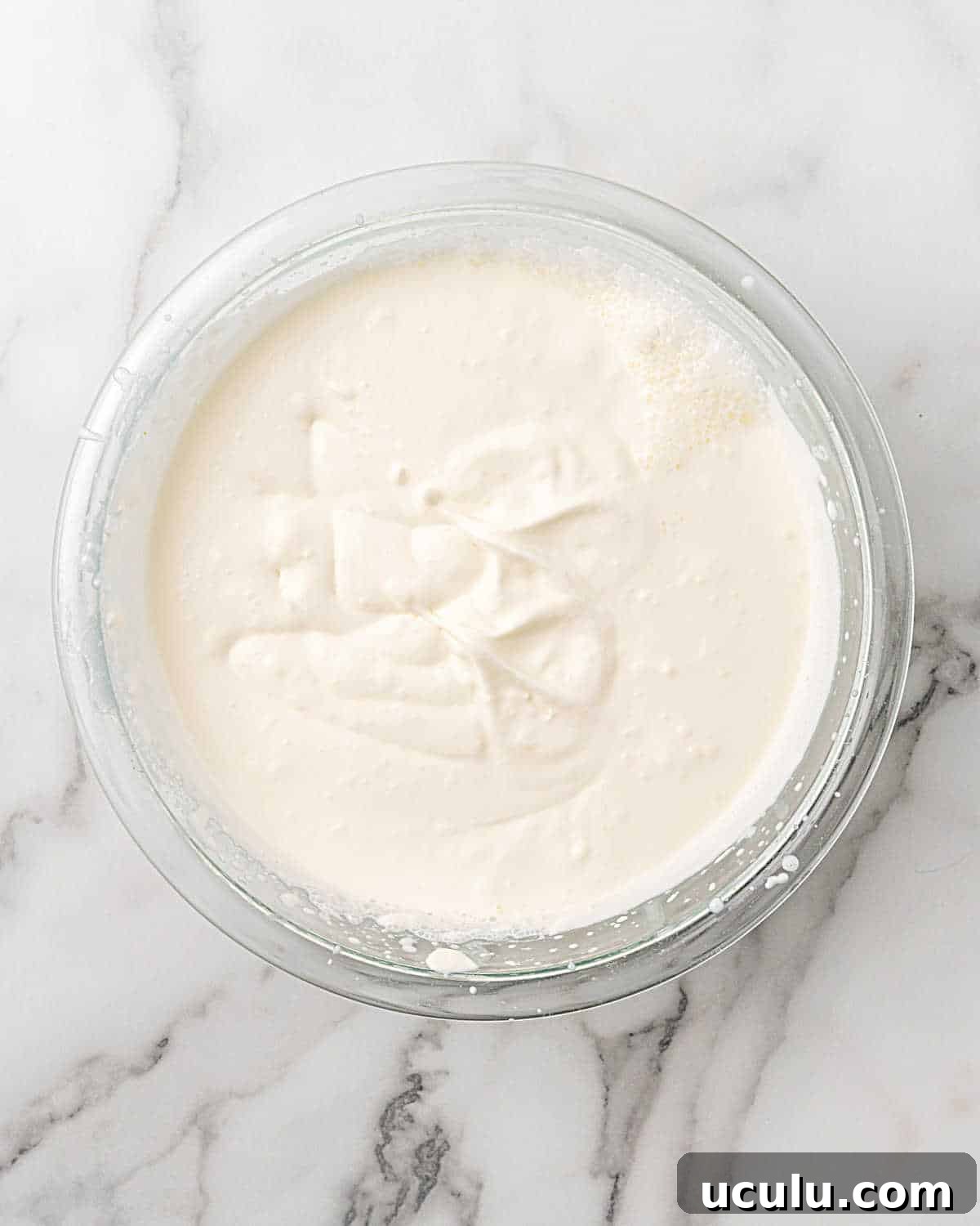 Glass bowl of whipped cream on a white and grey marble surface.