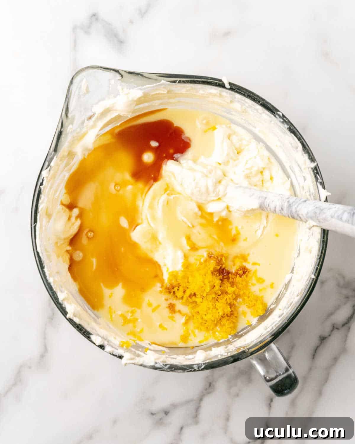 Cheesecake batter with flavorings in a glass jar on a white and grey marble surface.