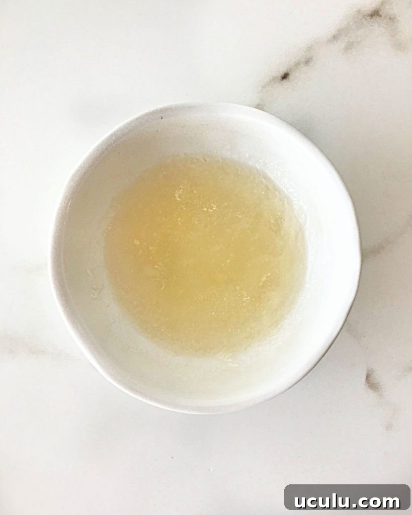 Small white bowl with hydrated gelatin on a white marble surface.