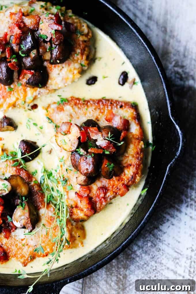 Pork chops in white wine cream sauce with mushrooms and bacon on top in a pan, overhead shot