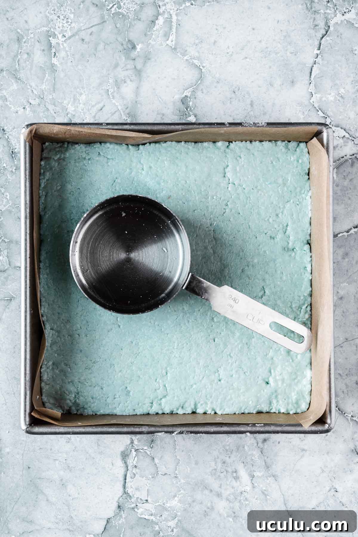 The blue top layer of candy being compacted with a measuring cup.