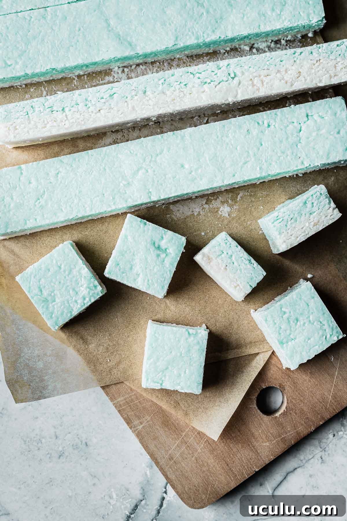 A cutting board with strips of coconut candy being cut into squares.