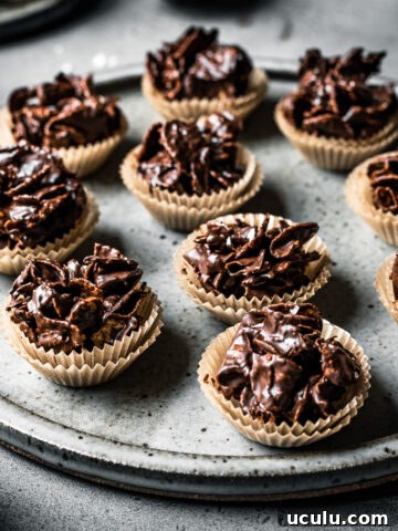 A side view of a large speckled grey ceramic plate holding chocolate covered cornflake cereal in doubled up mini brown paper cupcake liners.