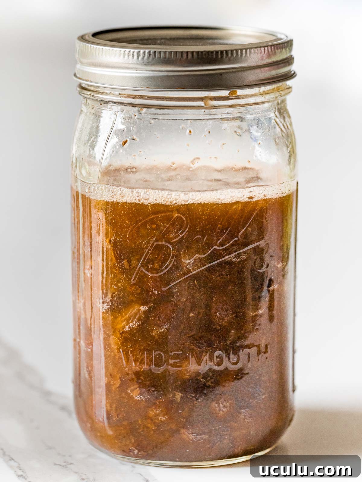 raisins fermenting in water with a foam layer on top inside a glass mason jar with a lid