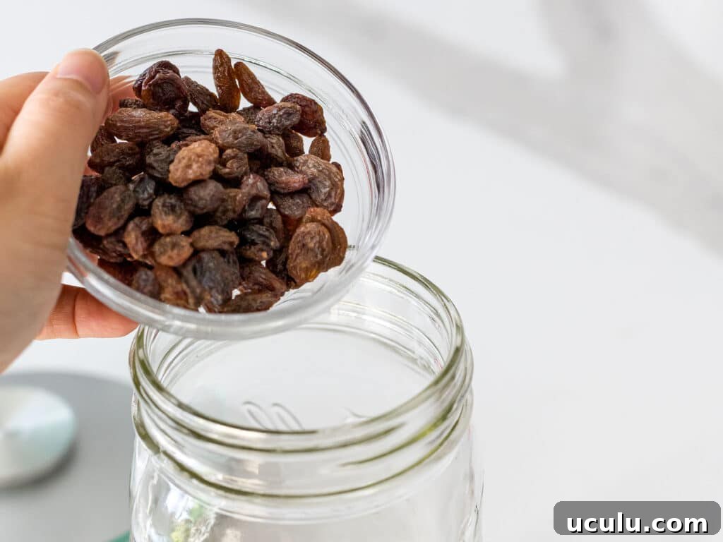 raisins being added to a glass mason jar