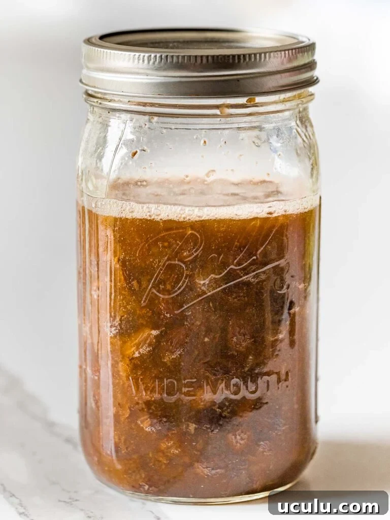 raisins fermenting in water with a foam layer on top inside a glass mason jar with a lid