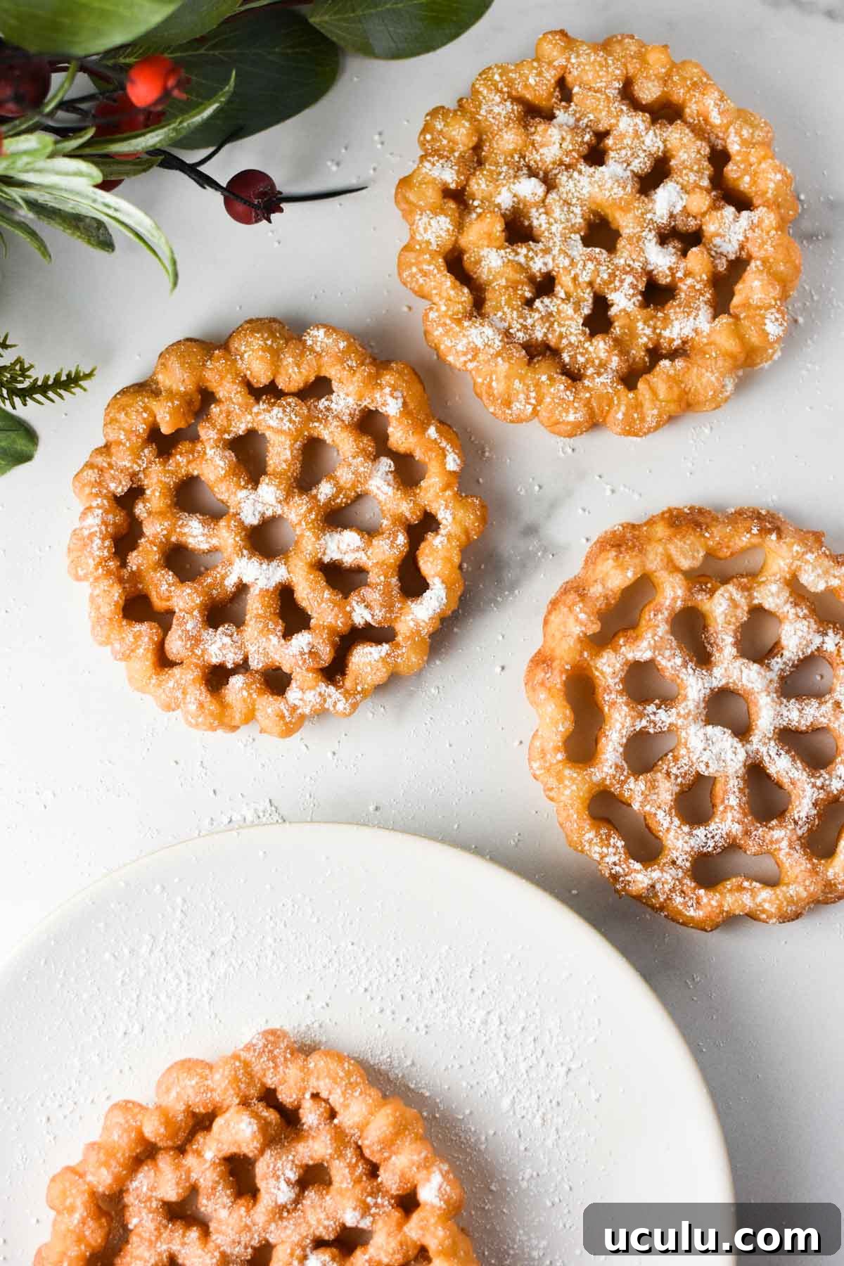 Three rosettes on a table with powdered sugar on top and a plate nearby.