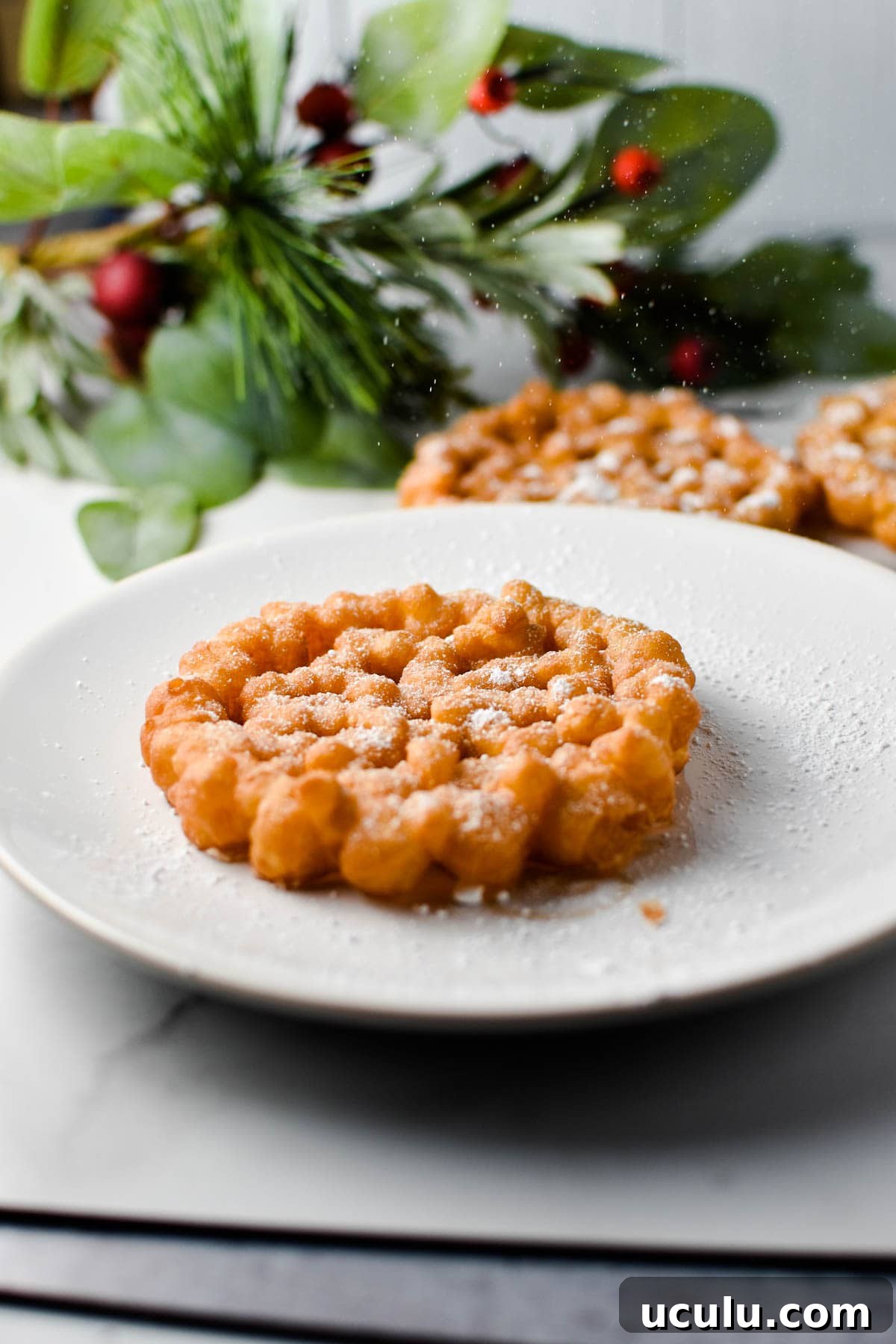 A snowflake cookie on a white plate being dusted with powdered sugar