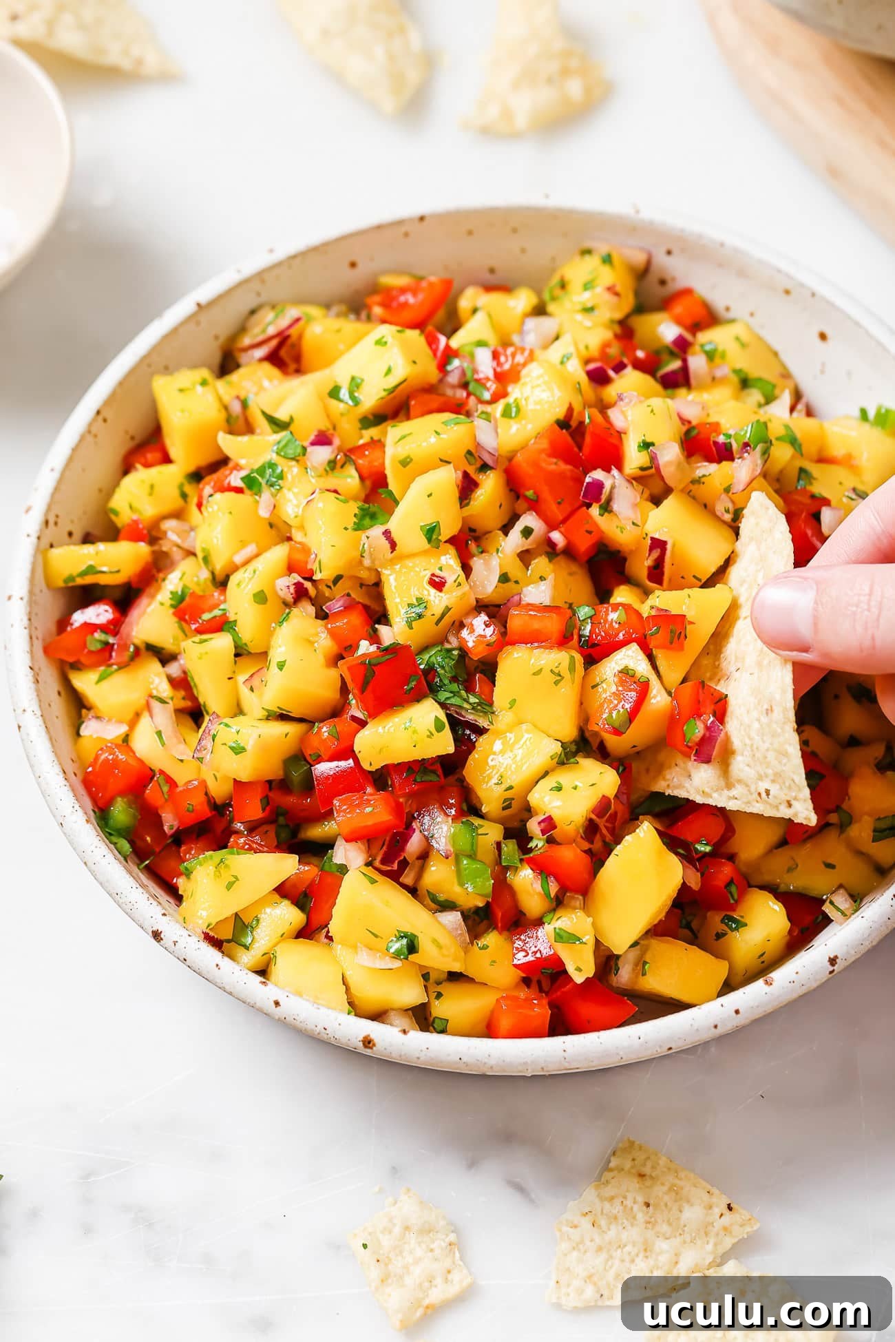 An overhead view of a chip scooping pineapple salsa out of a white bowl.