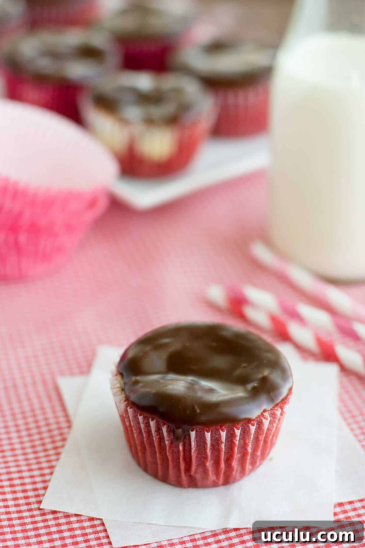 A red velvet cheesecake cupcake topped with chocolate ganache.