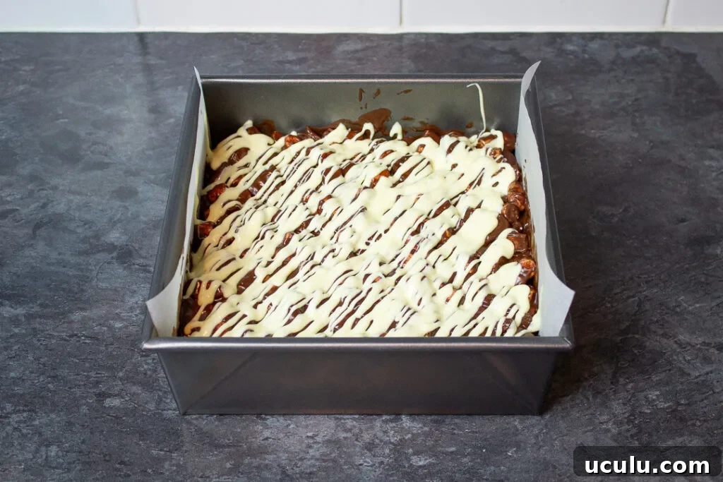 Melted white chocolate drizzled over the top of rocky road in a baking tray.
