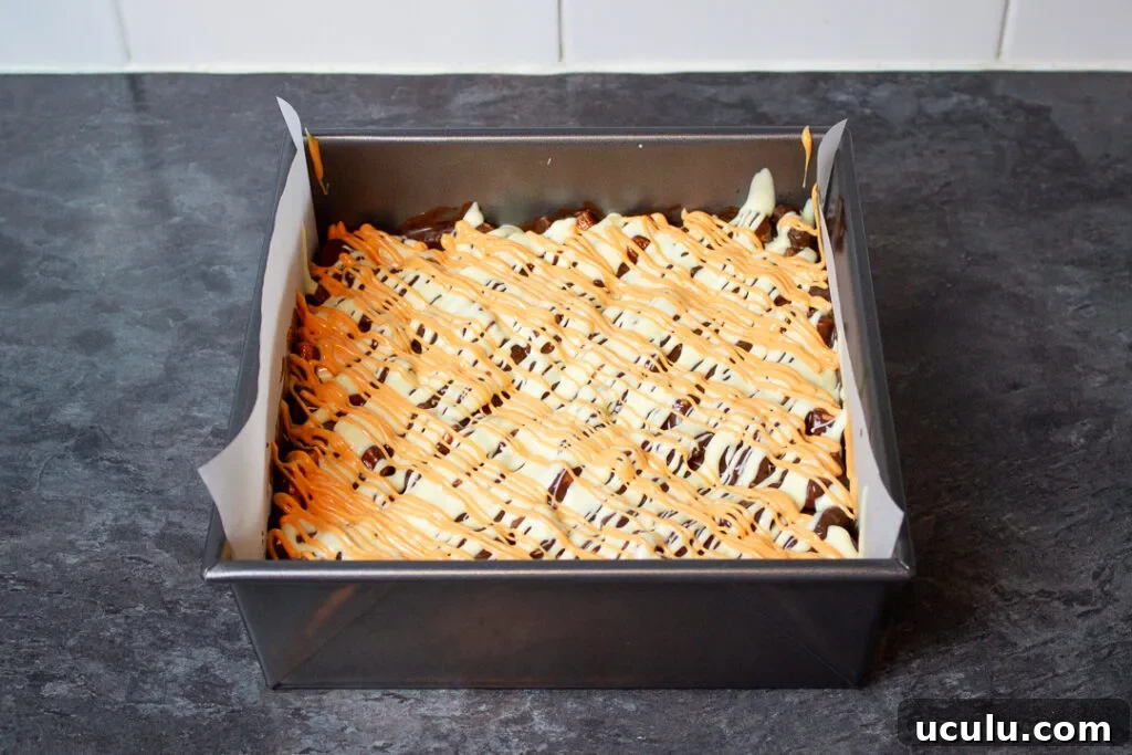 Melted orange coloured white chocolate drizzled over the top of rocky road in a baking tin.