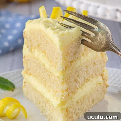 A slice of lemon layer cake with a fork cutting into it.