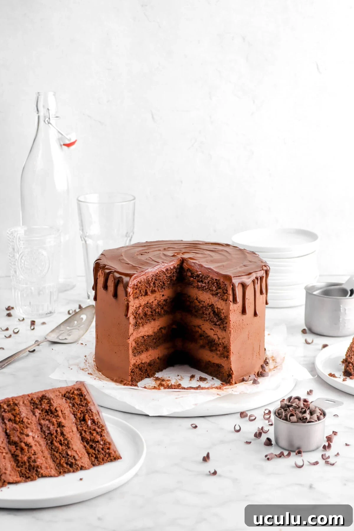 pulled back shot of chocolate layer cake on plate with two slices missing and on white plates beside cake