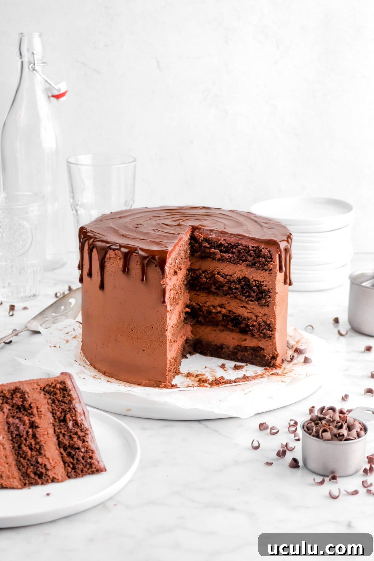 front shot of chocolate cake with slices missing on white plate with chocolate curls and cake server beside