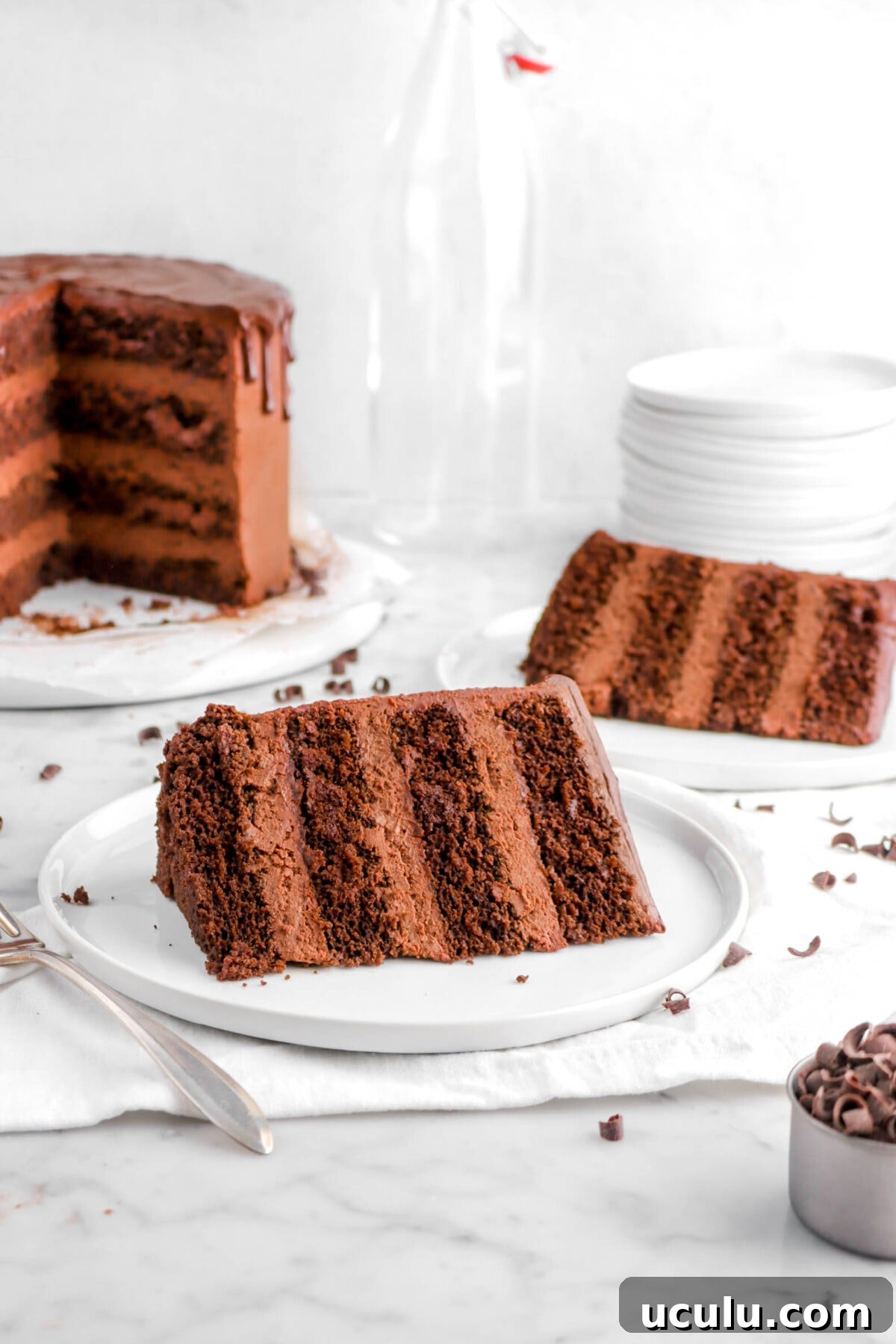 two slices of chocolate cake on white plates with cake behind