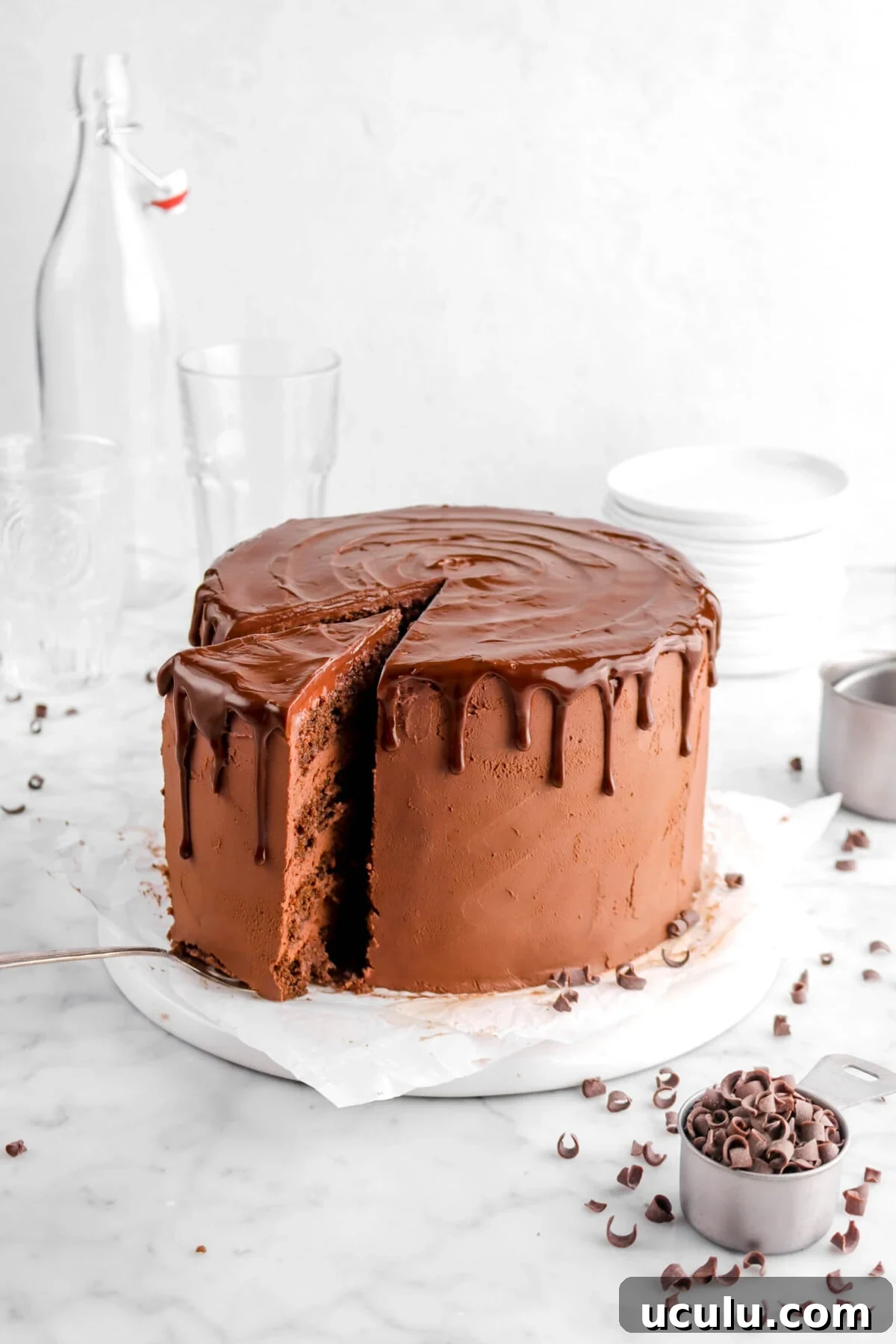slice of cake being pulled away on upside down white plate with a stack of white plates behind and empty glasses