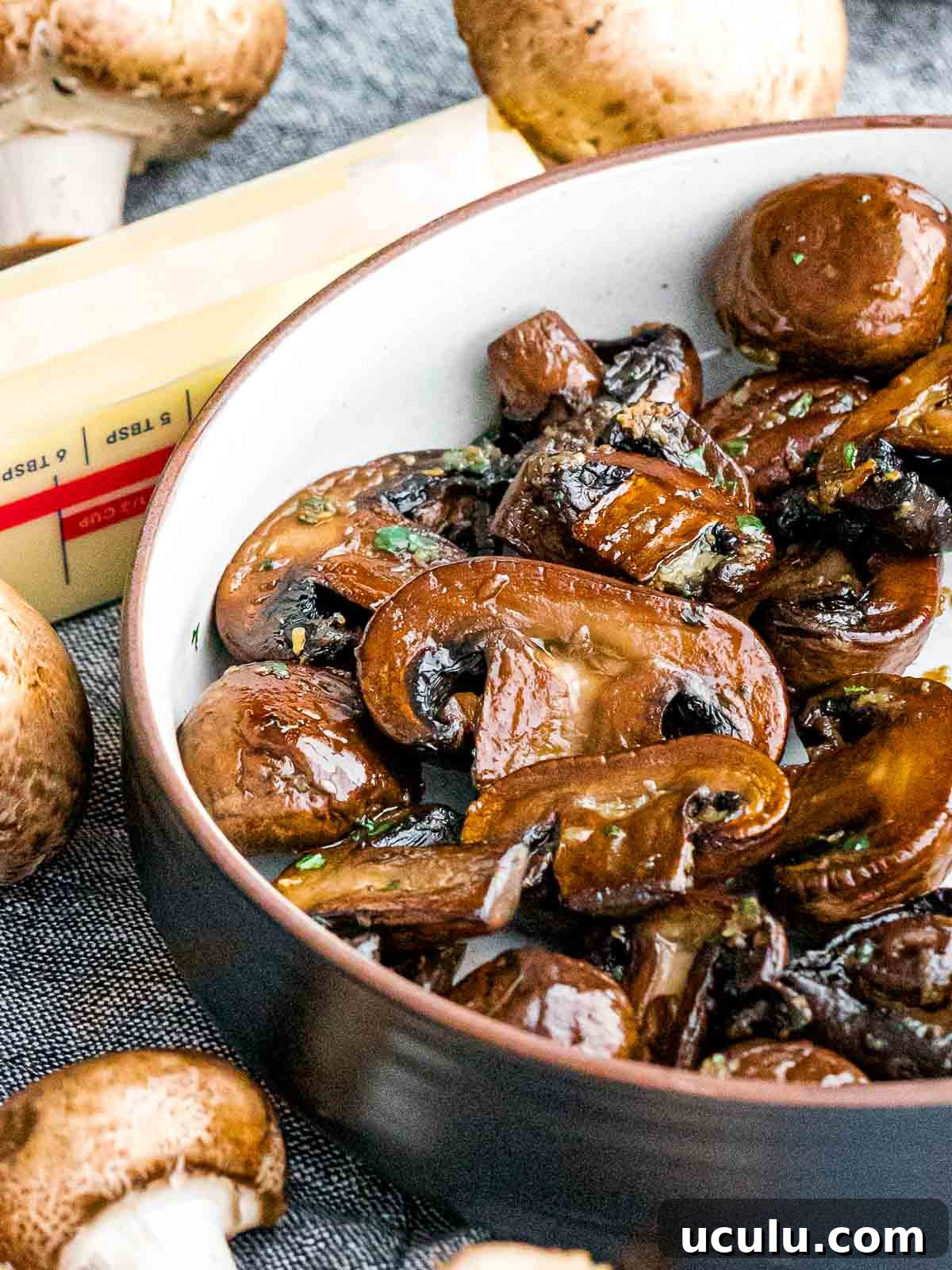 golden brown garlic butter mushrooms in a bowl next to a stick of butter