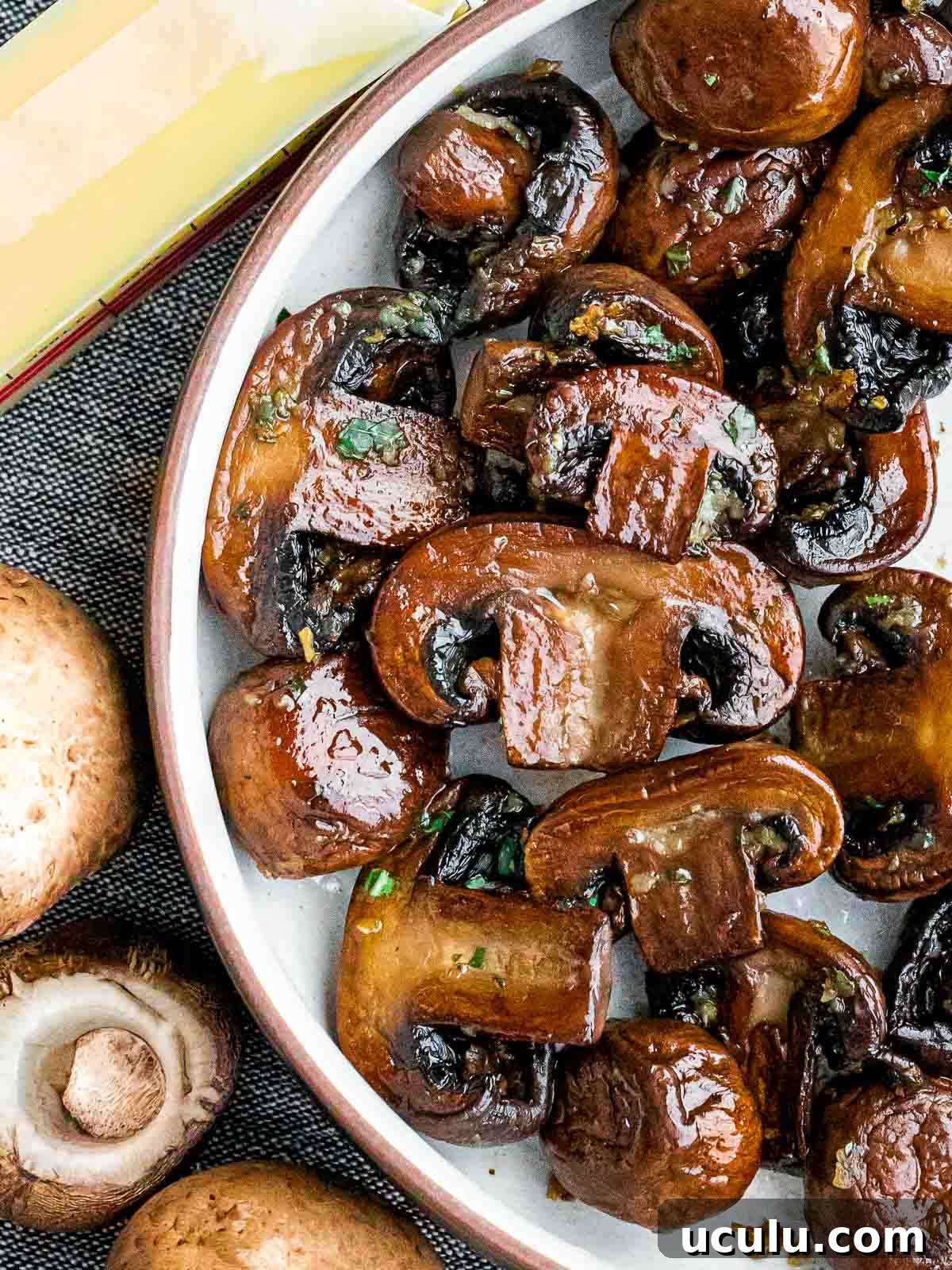 close up of sauteed mushrooms next to butter and uncooked mushrooms