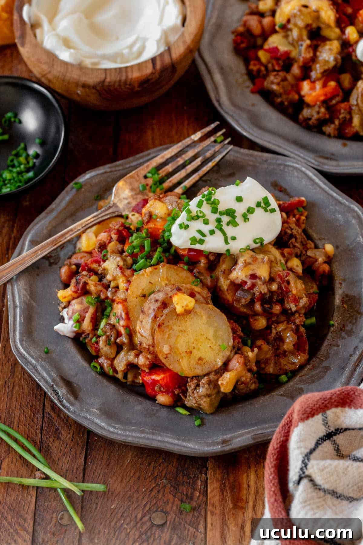 cowboy casserole on a plate with sour cream, chives, and a fork.