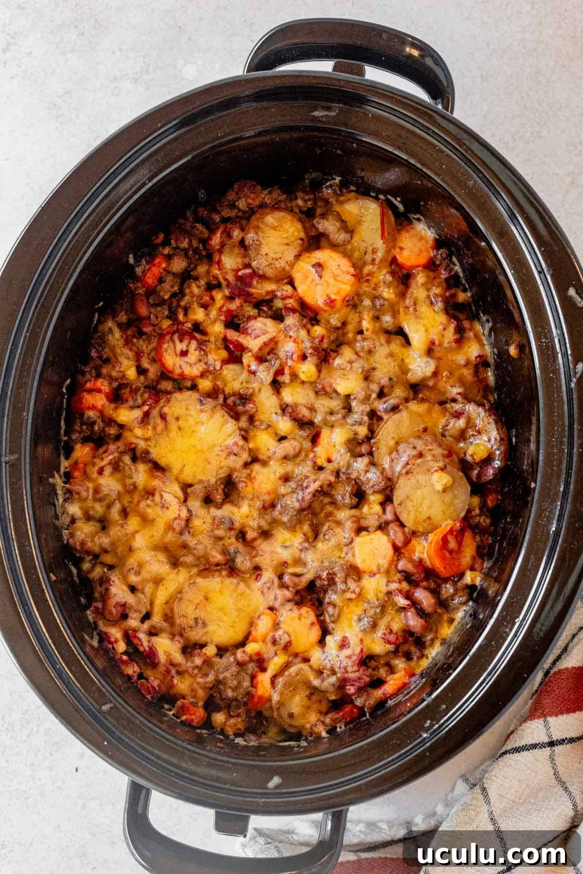 crock pot cowboy casserole cooked and topped with melted cheese.