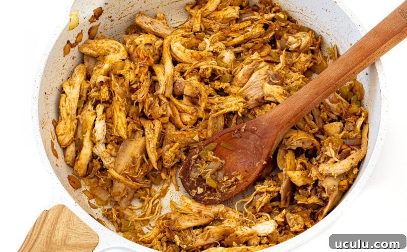 Shredded chicken added to the skillet with a wooden spoon stirring it.