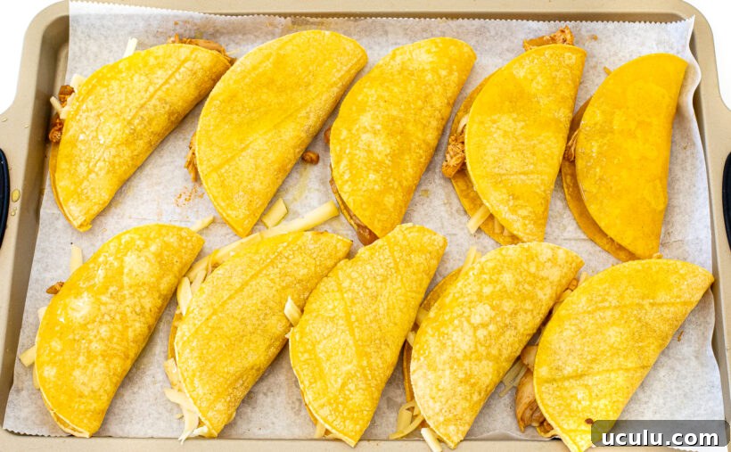 Crispy tacos filled with shredded chicken mixture and placed on a sheet pan.