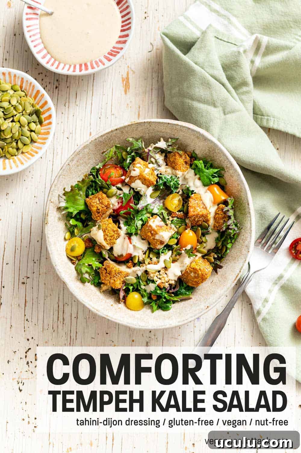 Comforting Tempeh Kale Salad in a ceramic bowl next to a green linen and fork