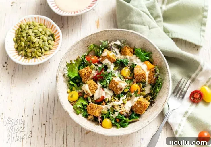 Comforting Tempeh Kale Salad in a ceramic bowl next to a green linen and fork
