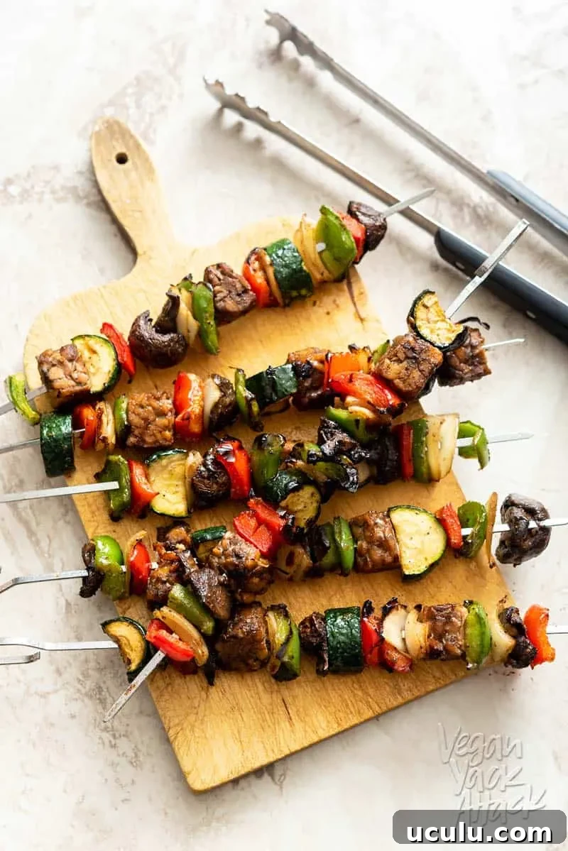 Tempeh veggie skewers stacked on a sandwich board with tongs next to them