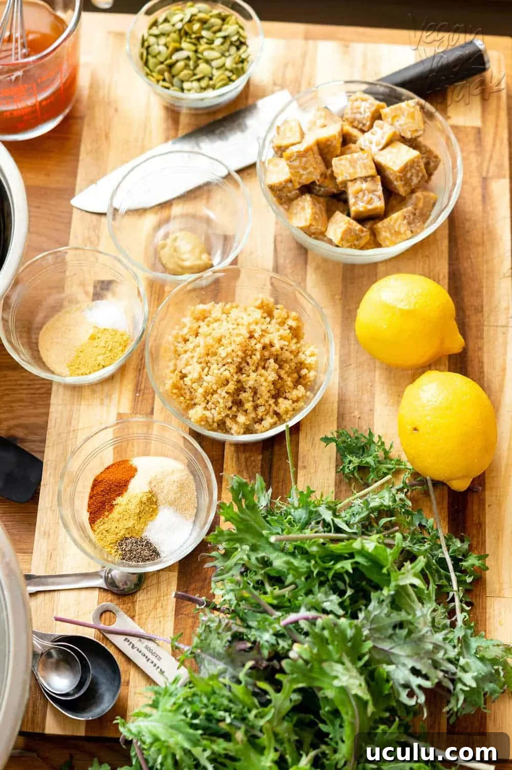 Ingredients such as tempeh, lemon, quinoa, spices, kale, and more laid out on a cutting board