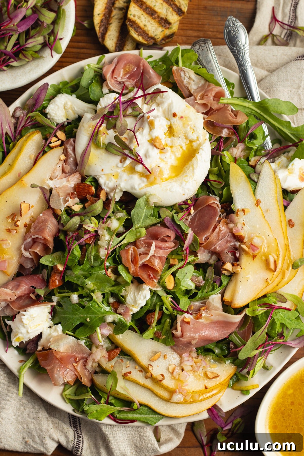 This is a picture of a plate filled with an arugula burrata salad with prosciutto and pear.