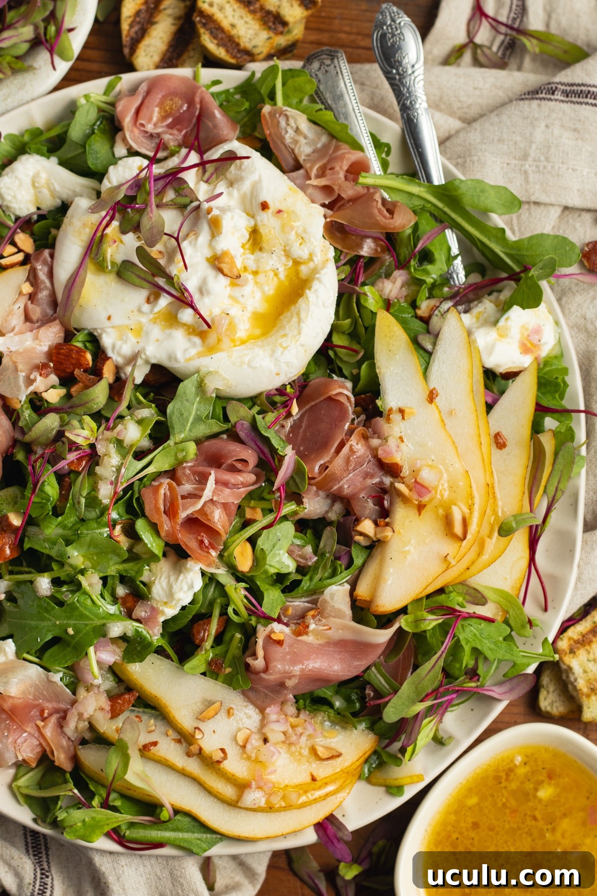 This is a picture of a plate filled with an arugula burrata salad with prosciutto and pear.