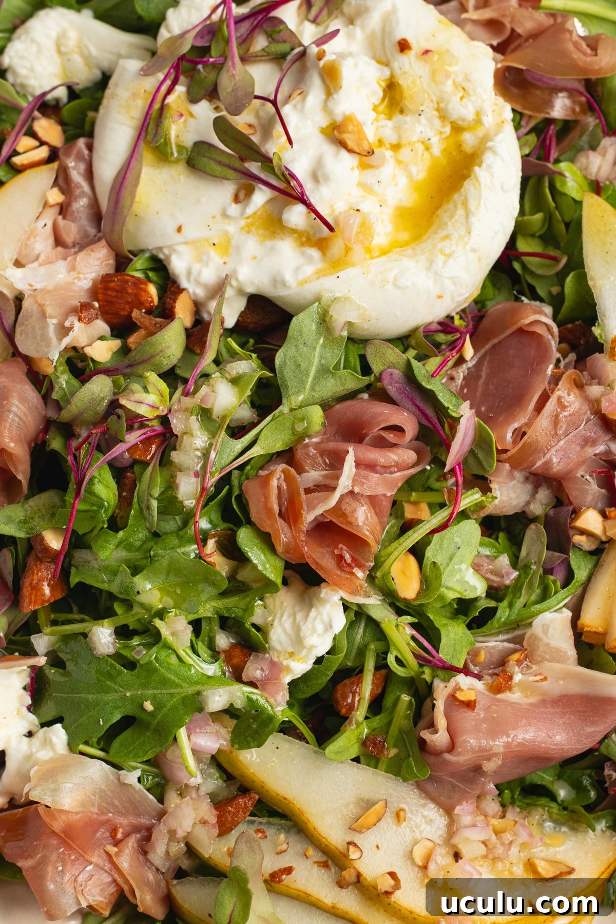 This is a picture of a plate filled with an arugula burrata salad with prosciutto and pear.