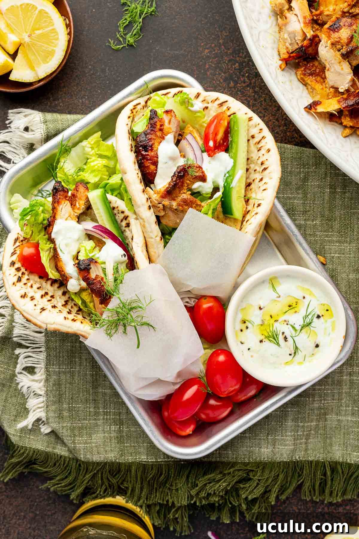 Two chicken shawarma with lettuce, tomato, cucumber, onion, and tzatziki in pita bread, served on a tray with cherry tomatoes and a small bowl of tzatziki sauce.