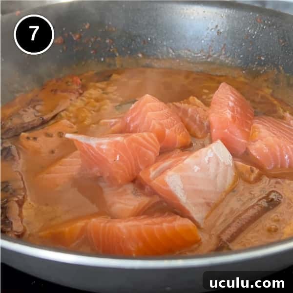 Fresh salmon being added to a coconut sauce