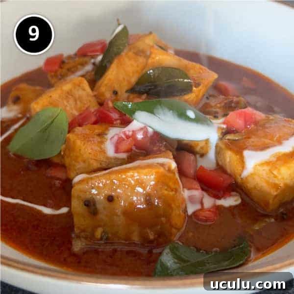 A bowl of Indian Salmon Curry decorated with fresh curry leaves, tomato and a drizzle of coconut cream