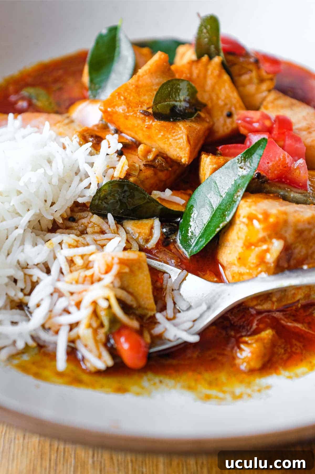 A bowl of Indian Salmon Curry and rice decorated with fresh curry leaves, tomato and a drizzle of coconut cream