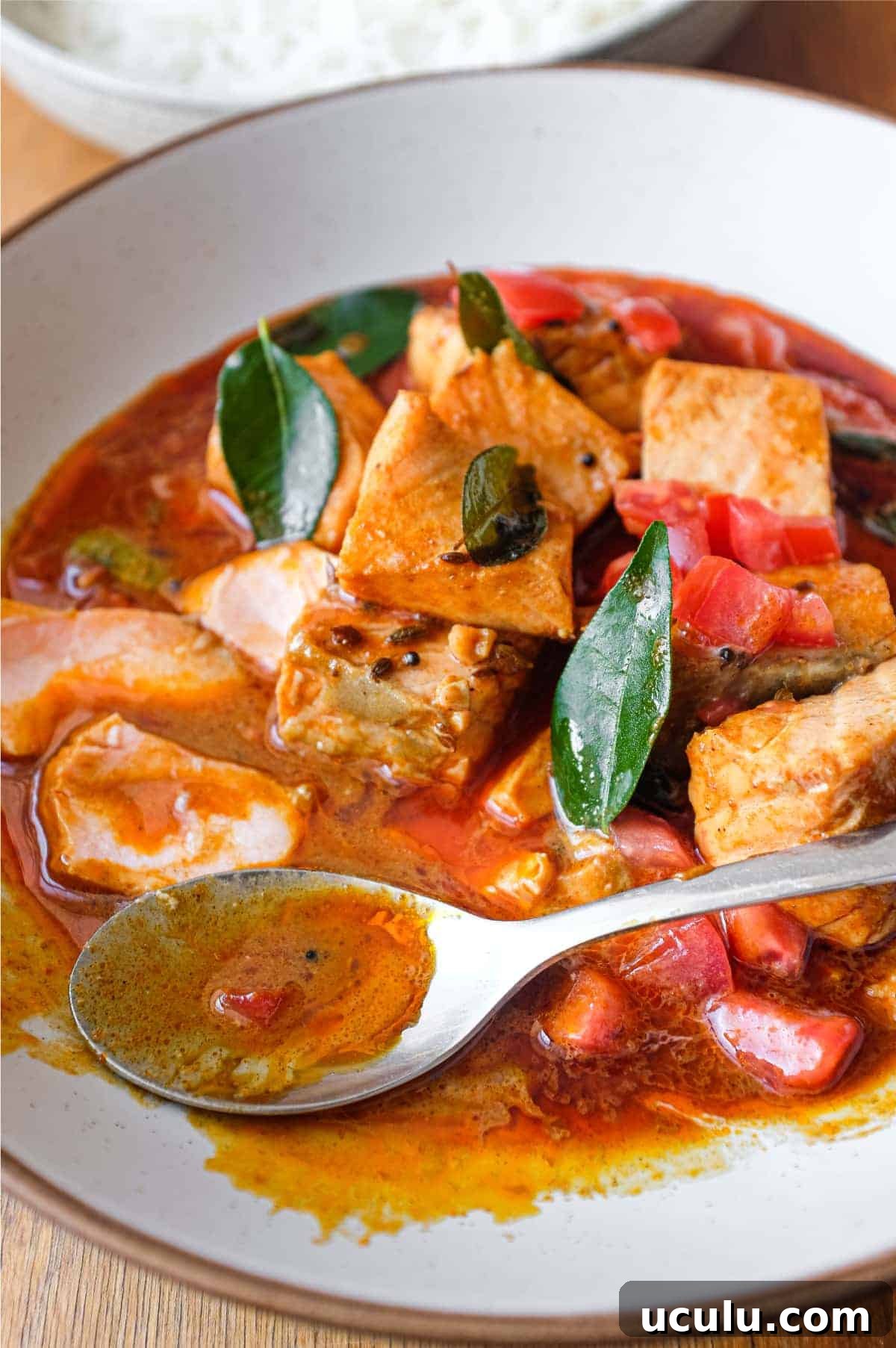 A bowl of Indian Salmon Curry decorated with fresh curry leaves, tomato and a drizzle of coconut cream