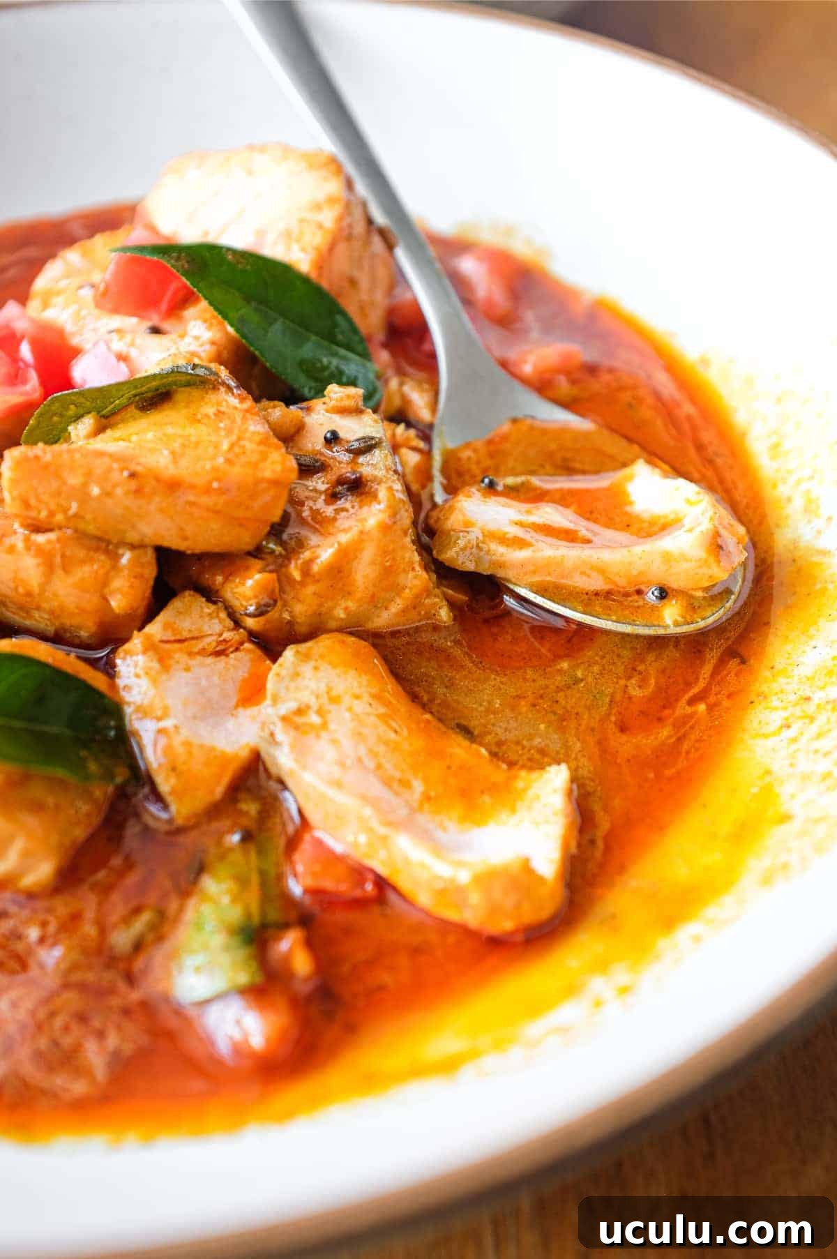 A bowl of Indian Salmon Curry decorated with fresh curry leaves, tomato and a drizzle of coconut cream