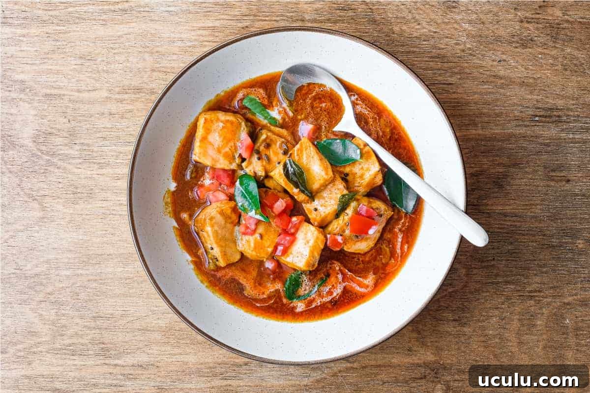 A bowl of Indian Salmon Curry decorated with fresh curry leaves, tomato and a drizzle of coconut cream
