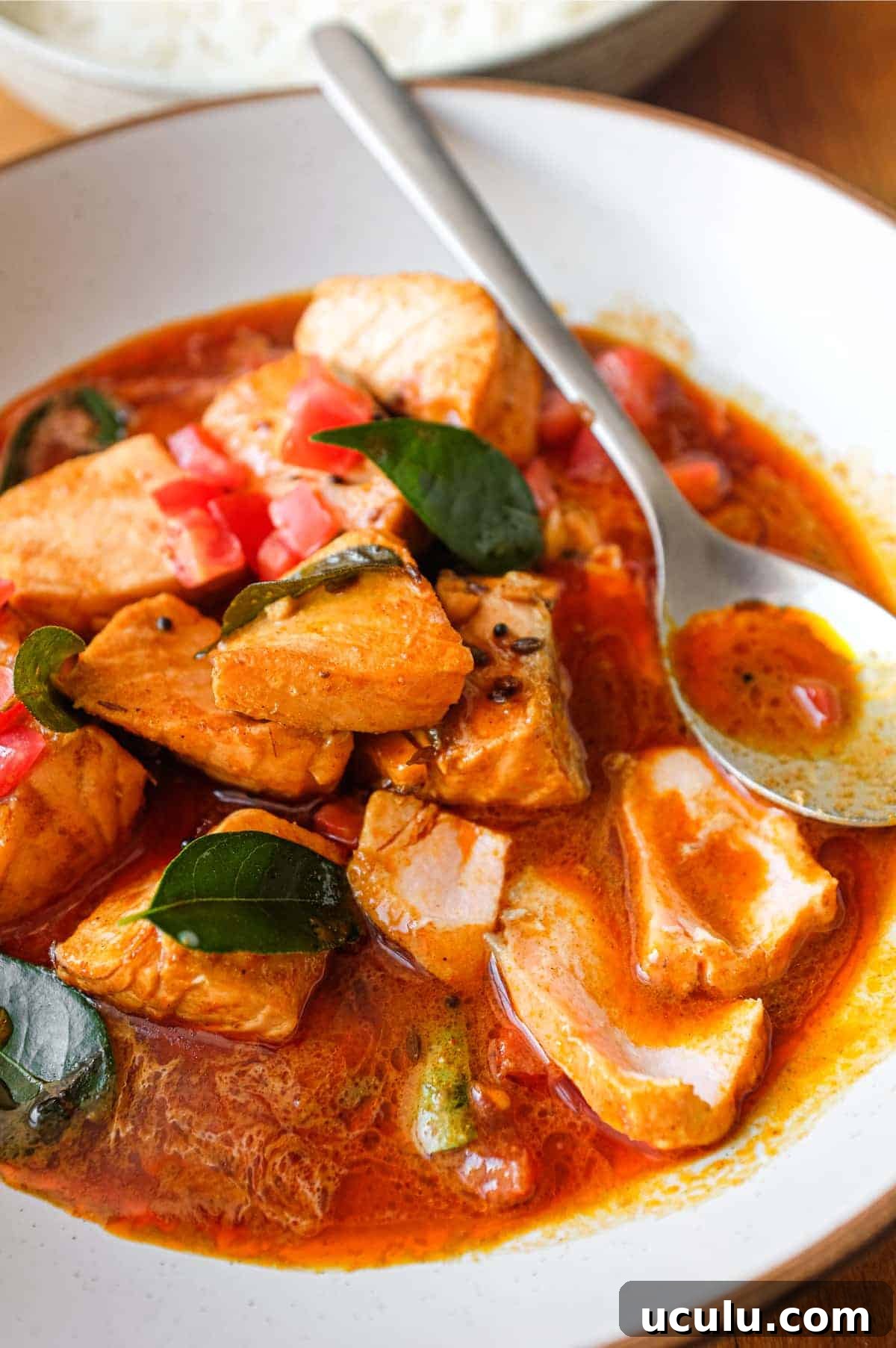 A bowl of Indian Salmon Curry decorated with fresh curry leaves, tomato and a drizzle of coconut cream