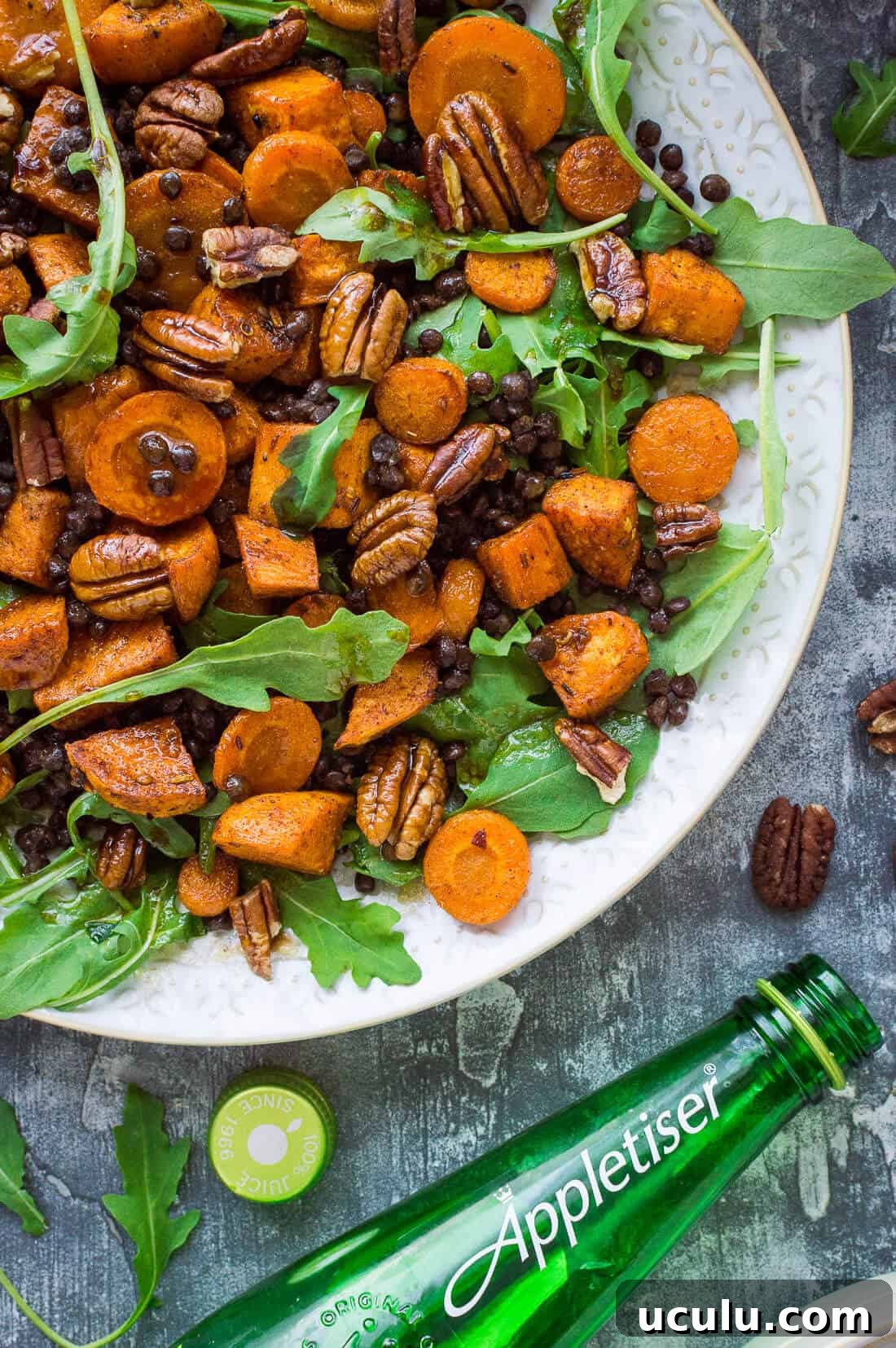 A close up of a plate of roasted sweet potato, lentil and rocket salad with a bottle of Appletiser