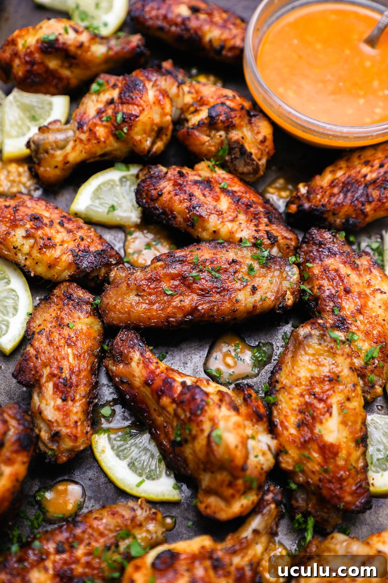 A large baking tray filled with lemon garlic chicken wings sitting next to a bowl of lemon garlic marinade