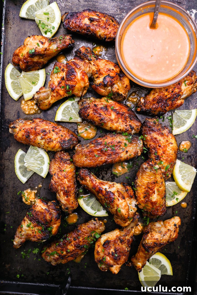 Lemon garlic chicken wings sitting on a serving tray with fresh lemon wedges garnished with chopped parsley