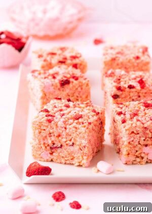 Six rice krispie treats on a white tray with scattered pieces of freeze-dried strawberry, text reads "strawberry rice krispie treats".