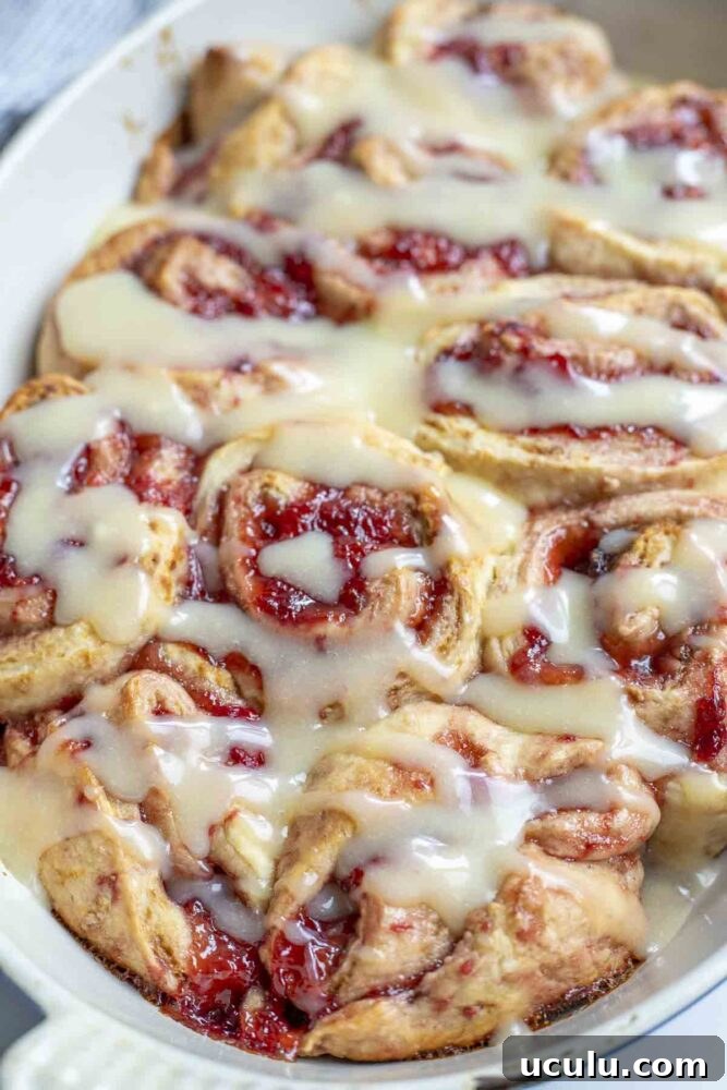 white oval baking dish with sourdough strawberry rolls topped with cream cheese frosting.