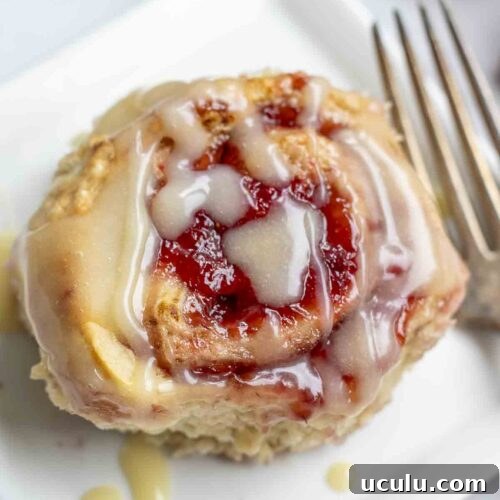 overhead photo of a sourdough strawberry sweet roll drizzled with icing on a white square plate with a antique fork to the right