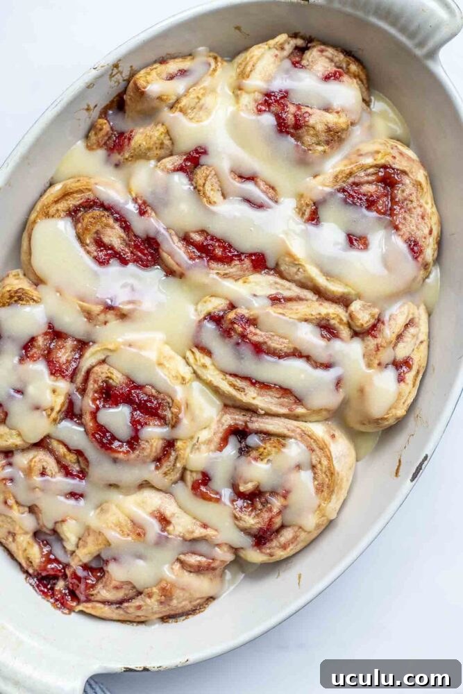 overhead photo of a oval baking dish full of sourdough strawberry rolls topped with cream cheese icing.
