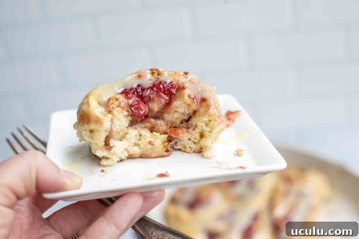 hand holding up a white plate with a strawberry roll with a bite taken out
